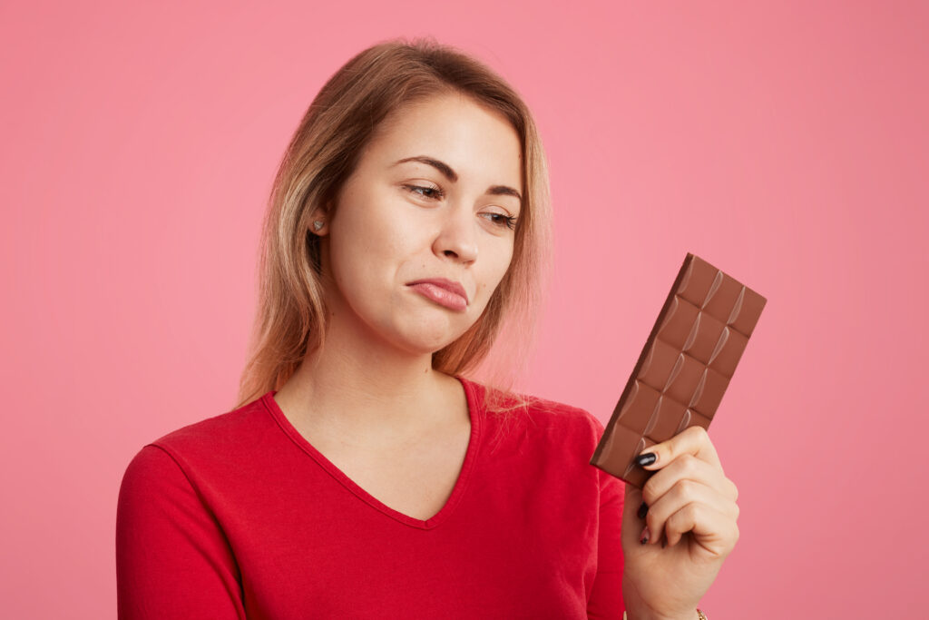 woman looks with-discontent expression sweet bar chocolate keeps To Avoid for Weight Loss