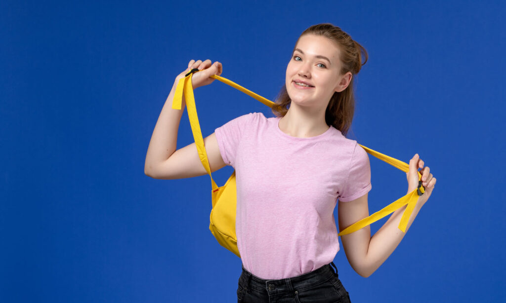 front-view-young-female-pink-t-shirt-holding-yellow-backpack-just-smiling-blue-wall